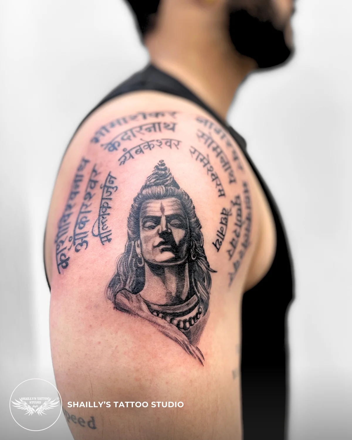 Detailed Shiva portrait and Sanskrit script tattoo on an upper arm