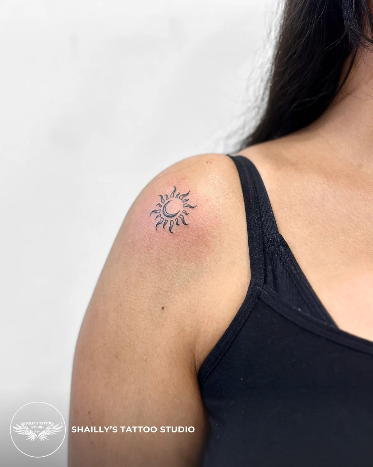 Small fine-line sun symbol tattoo on a shoulder