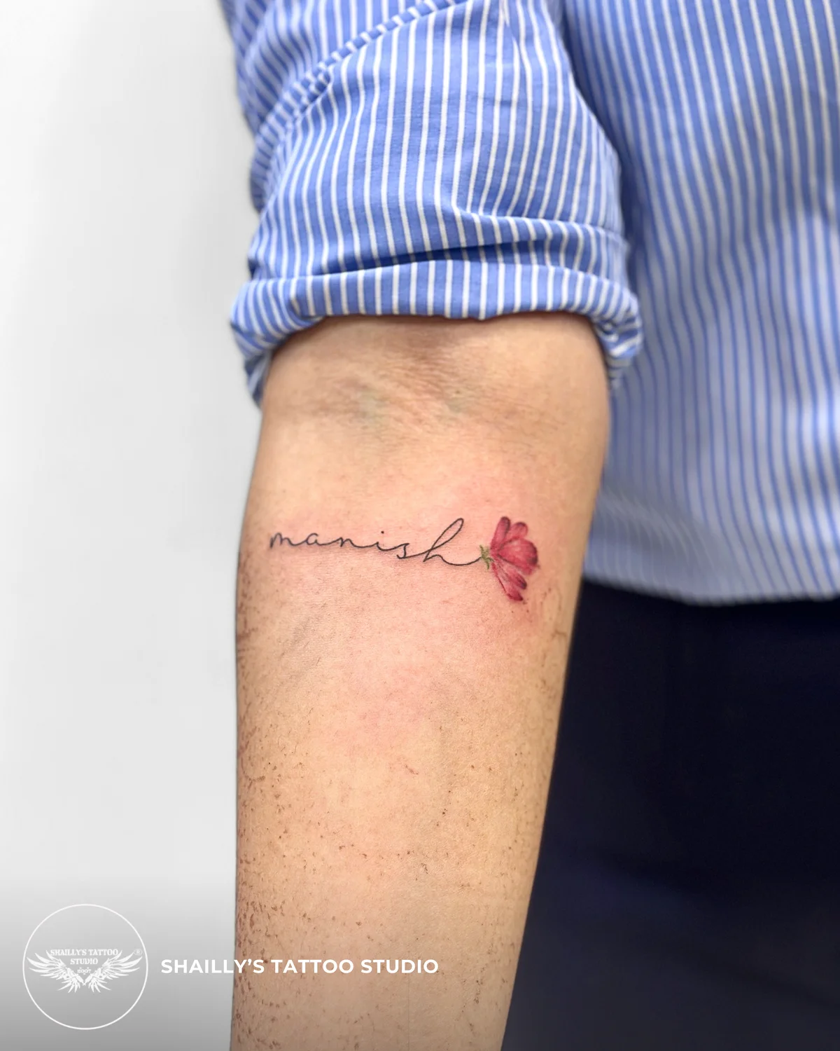 Fine-line name tattoo finished with a small red rose